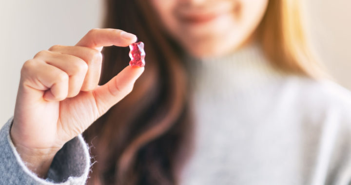 Closeup image of a beautiful woman holding and looking at a red gummy bear