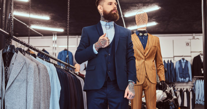 Elegantly dressed bearded shop assistant with standing near mannequin in menswear store.